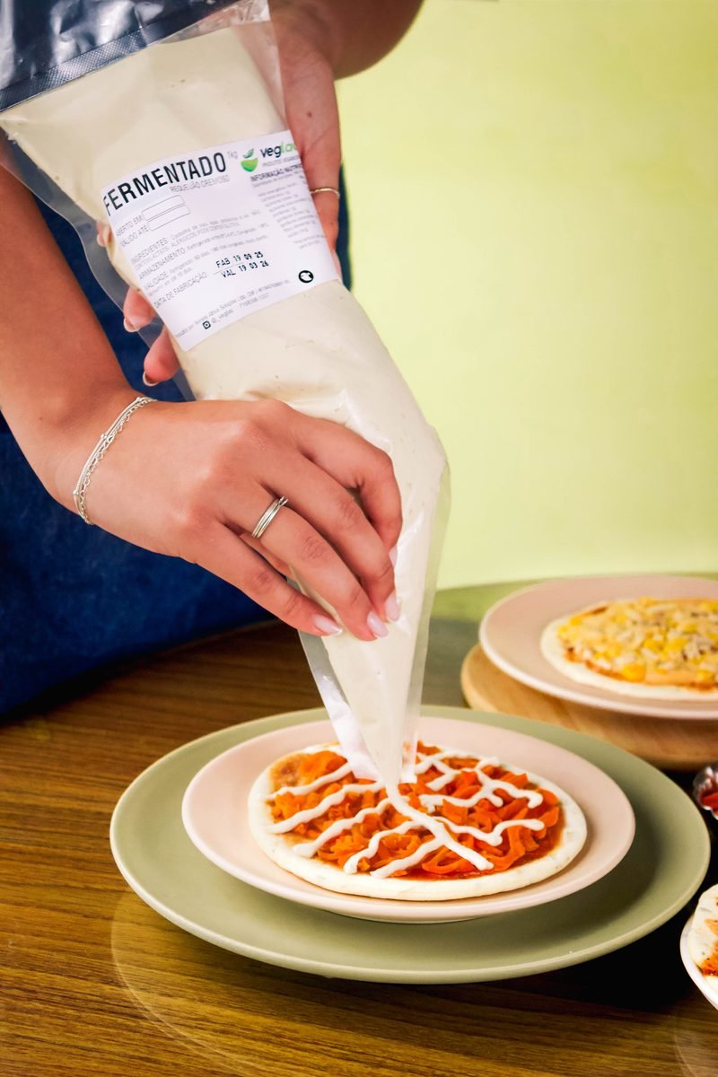 Mini pizza vegana sendo finalizada com molho cremoso Veglac